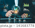 Businessman holding digital magnifying glass over coins with interactive financial dashboard overlay, investment management and asset allocation. 141683778