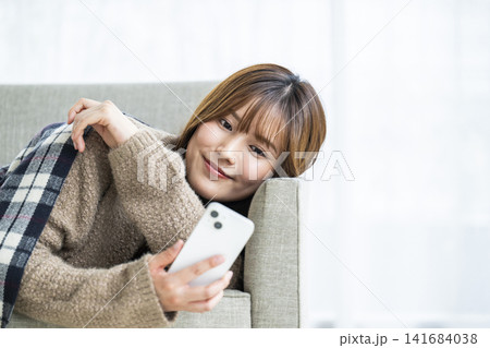 ソファーに横になってスマホを見る若い女性 141684038