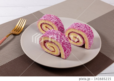 slices of purple sweet potato cake roll with coconut flakes and berry jam filling on dark background, gourmet dessert slices of purple sweet potato cake roll with coconut flakes and berry jam filling on dark background, gourmet dessert 141685215