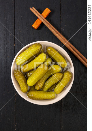 bowl of crunchy Russian pickled cucumbers gherkins with brine and chopsticks on dark wooden table, traditional appetizer bowl of crunchy Russian pickled cucumbers gherkins with brine and chopsticks on dark wooden table, traditional appetizer 141685225