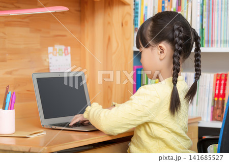 Asian little girl using laptop at wooden desk, back view child learning at home, online education concept 141685527