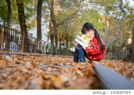 Asian girl reading book on railway track in autumn park, focused emotion, education and peaceful outdoor learning concept 141685564