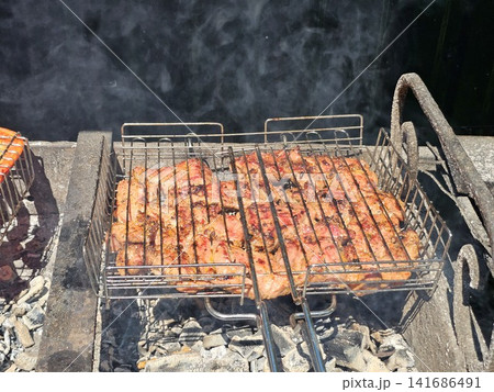 Juicy pork steaks grilling on metal barbecue grate over hot charcoal during sunny outdoor barbecue cooking Juicy pork steaks grilling on metal barbecue grate over hot charcoal during sunny outdoor barbecue cooking 141686491