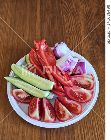 Fresh vegetable salad with sliced tomatoes cucumbers sweet pepper and red onion served on a white plastic plate outdoors Fresh vegetable salad with sliced tomatoes cucumbers sweet pepper and red onion served on a white plastic plate outdoors 141686499