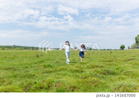 Two friends holding hands and running joyfully through a wide green grass field. Two friends holding hands and running joyfully through a wide green grass field. 141687000