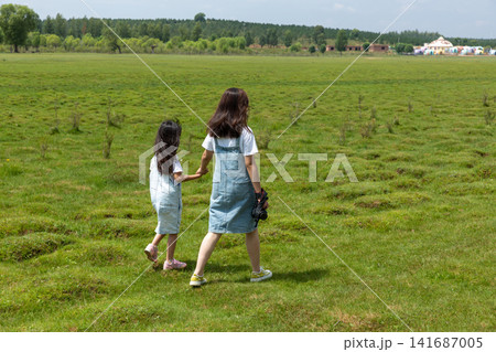 The backs of two Asian girls carrying DSLR cameras walking on the grassland The backs of two Asian girls carrying DSLR cameras walking on the grassland 141687005