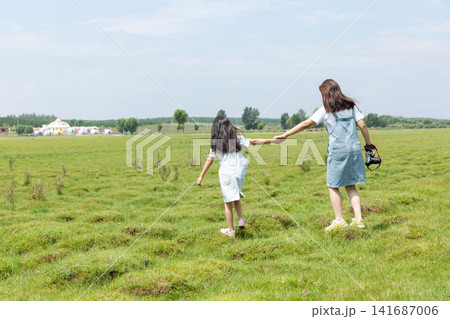 The backs of two Asian girls carrying DSLR cameras walking on the grassland The backs of two Asian girls carrying DSLR cameras walking on the grassland 141687006