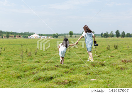 The backs of two Asian girls carrying DSLR cameras walking on the grassland The backs of two Asian girls carrying DSLR cameras walking on the grassland 141687007