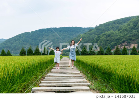 Two girls held hands and ran along the path in the fields. Two girls held hands and ran along the path in the fields. 141687033