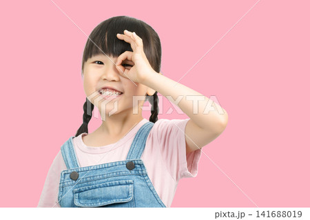 Cute little girl making OK sign over her eye looking at camera 141688019