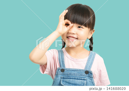 Cute little girl making OK sign over her eye looking at camera 141688020