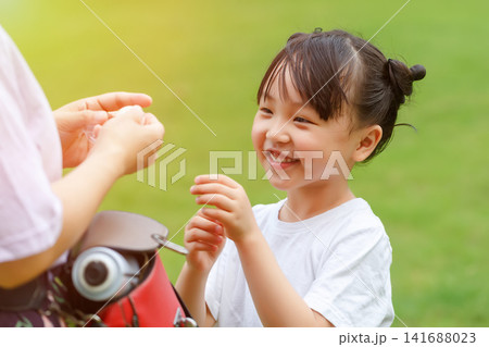 Cute little girl looking at mother asking for snacks or sweets with happy smile in park 141688023