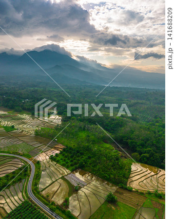 Aerial view of Sapa rice terraces at sunrise with golden light over green fields and misty mountain valleys Aerial view of Sapa rice terraces at sunrise with golden light over green fields and misty mountain valleys 141688209