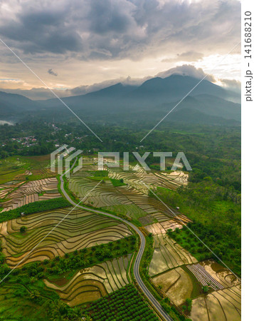 Aerial view of Sapa rice terraces at sunrise with golden light over green fields and misty mountain valleys Aerial view of Sapa rice terraces at sunrise with golden light over green fields and misty mountain valleys 141688210