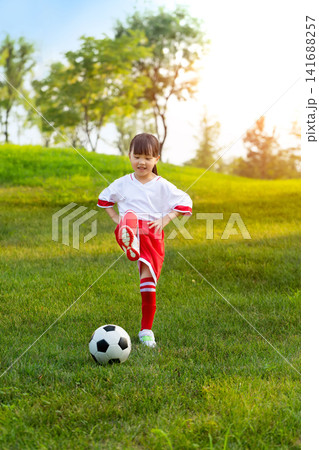 Smiling young girl dribbling a classic soccer ball on a lush green lawn surrounded by trees. Smiling young girl dribbling a classic soccer ball on a lush green lawn surrounded by trees. 141688257