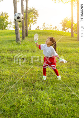 Enthusiastic young goalkeeper wearing gloves and catching a soccer ball in mid-air at the park. 141688269