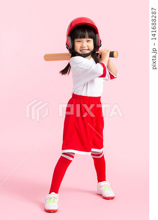 Full length shot of a young girl swinging a wooden baseball bat against a solid pink background. Full length shot of a young girl swinging a wooden baseball bat against a solid pink background. 141688287
