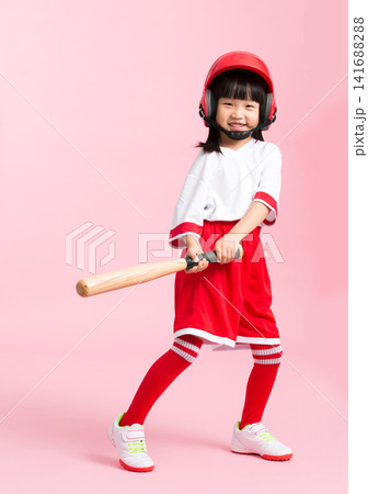 Full length shot of a young girl swinging a wooden baseball bat against a solid pink background. Full length shot of a young girl swinging a wooden baseball bat against a solid pink background. 141688288