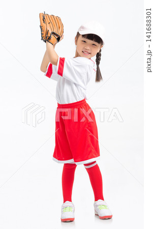 Full length view of a young baseball player raising her gloved hand against a white backdrop. Full length view of a young baseball player raising her gloved hand against a white backdrop. 141688301