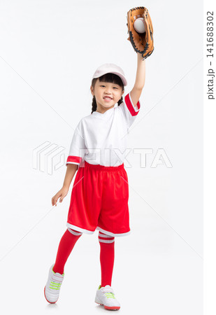 Full length view of a young baseball player raising her gloved hand against a white backdrop. Full length view of a young baseball player raising her gloved hand against a white backdrop. 141688302