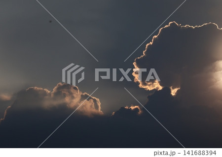 黒い雲の中に太陽のオレンジの光りが漏れている空の風景 141688394