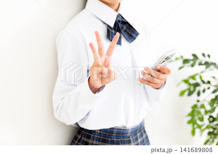 スマートフォンを持って指を3本立てる制服姿の女子中学生 141689808