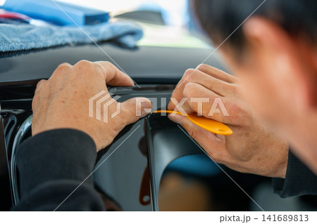 A car wrapping specialist applies a polyurethane film to the car. Detailer PPF A car wrapping specialist applies a polyurethane film to the car. Detailer PPF 141689813