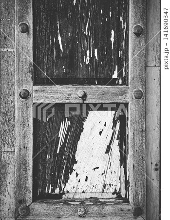 Black and white closeup of antique weathered wooden window frame with peeling paint and round wooden pegs, rustic vintage architecture background. Black and white closeup of antique weathered wooden window frame with peeling paint and round wooden pegs, rustic vintage architecture background. 141690347