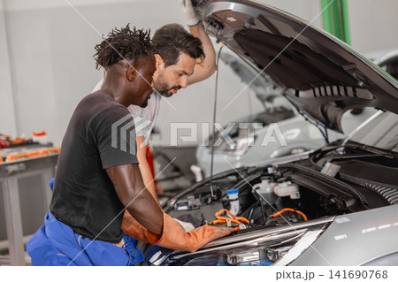 Professional EV Car Service, Male workers Electricity Vehicle Fix Maintenance in EV Garage workshop. Professional EV Car Service, Male workers Electricity Vehicle Fix Maintenance in EV Garage workshop. 141690768
