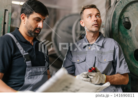 Engineer male workers team working service maintenance machine looking at blueprint in workshop, Heavy industry plant factory technician. Engineer male workers team working service maintenance machine looking at blueprint in workshop, Heavy industry plant factory technician. 141690811