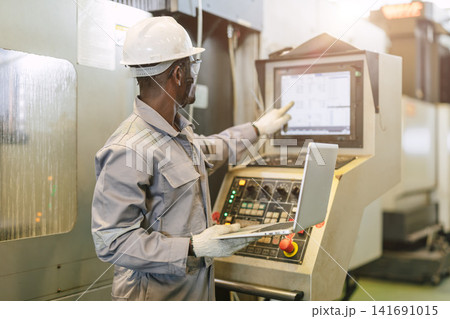 Professional engineer black male worker control operate CNC Machine in heavy industry metal factory Professional engineer black male worker control operate CNC Machine in heavy industry metal factory 141691015