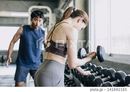 Healthy strong woman lifting high weight dumbbell a man looking amaze shock exciting pose Healthy strong woman lifting high weight dumbbell a man looking amaze shock exciting pose 141691183