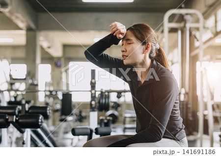 Sport woman tired exhausted fatigue sweating in sport fitness gym impact from heatwave hot condition Sport woman tired exhausted fatigue sweating in sport fitness gym impact from heatwave hot condition 141691186