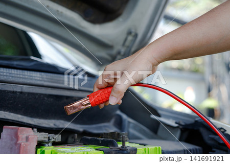 Hand holding jumper cable clamp near car battery 141691921