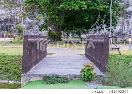 Small pedestrian bridge leading through lush garden trees walking paths peaceful outdoor atmosphere ideal for nature recreation travel landscape themes Small pedestrian bridge leading through lush garden trees walking paths peaceful outdoor atmosphere ideal for nature recreation travel landscape themes 141692262