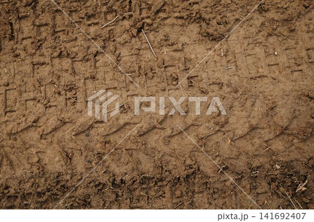 Close up of muddy ground with visible tire tread marks and soil texture. Abstract natural background with pattern and earth detail. Close up of muddy ground with visible tire tread marks and soil texture. Abstract natural background with pattern and earth detail. 141692407