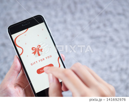 スマホに表示されたソーシャルギフト（eギフト）と女性の手元。画面はオリジナル制作 141692976