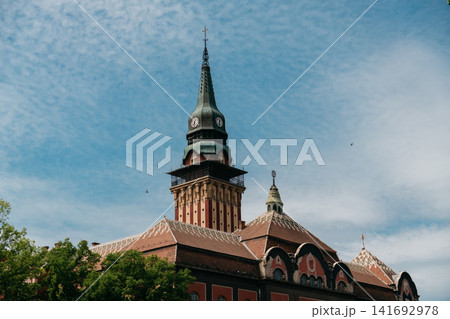 The iconic clock tower of Subotica City Hall stands above tiled rooftops in Subotica, Serbia. Historic architecture, urban heritage, and European travel destination appeal The iconic clock tower of Subotica City Hall stands above tiled rooftops in Subotica, Serbia. Historic architecture, urban heritage, and European travel destination appeal 141692978
