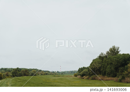 Open spring meadow with distant industrial chimney and tree line in the Belgrade suburb, Serbia. Concept of rural landscape, urban edge, and contrast between nature and industry Open spring meadow with distant industrial chimney and tree line in the Belgrade suburb, Serbia. Concept of rural landscape, urban edge, and contrast between nature and industry 141693006