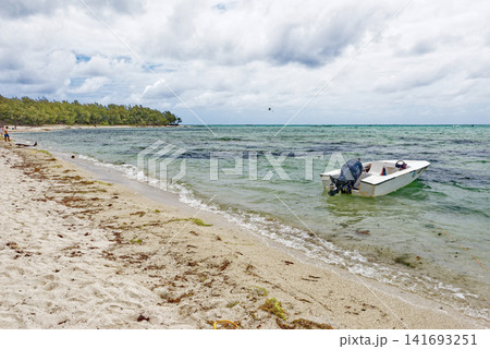 Small motorboat anchored in the shallow turquoise water near a sandy tropical beach at Ile aux Cerfs, Mauritius 141693251