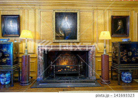 An antique marble fireplace with historical portraits and lacquer cabinets in the Great Hall at Dyrham Park, England 141693323
