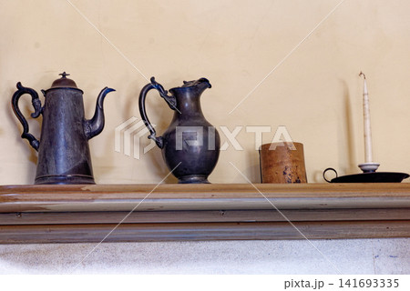 Antique pewter metalware and a white enamel pitcher on a wooden kitchen mantelpiece at Dyrham Park Antique pewter metalware and a white enamel pitcher on a wooden kitchen mantelpiece at Dyrham Park 141693335