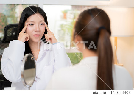 Asian woman doctor pointing at her face and eyes explaining skincare treatment and beauty. Asian woman doctor pointing at her face and eyes explaining skincare treatment and beauty. 141693408