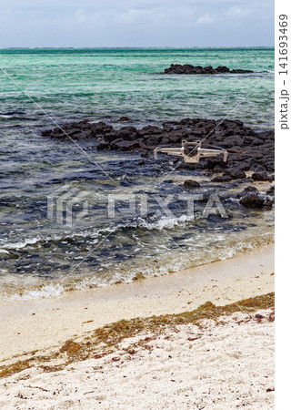 Camera drone hovering over a rocky volcanic shoreline and turquoise sea at Ile aux Cerfs, Mauritius Camera drone hovering over a rocky volcanic shoreline and turquoise sea at Ile aux Cerfs, Mauritius 141693469