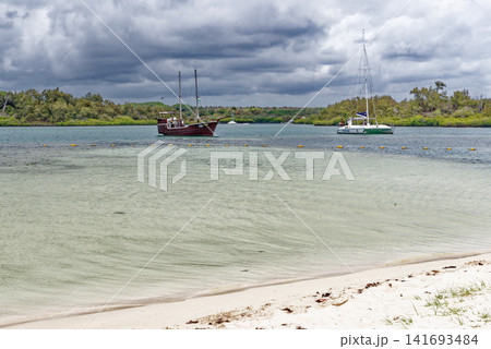 Traditional pirate style boat and a modern catamaran anchored in a tropical lagoon channel at Ile aux Cerfs, Mauritius Traditional pirate style boat and a modern catamaran anchored in a tropical lagoon channel at Ile aux Cerfs, Mauritius 141693484