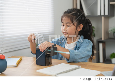 Young girl using manual pencil sharpener at wooden desk for schoolwork in bright home study space Young girl using manual pencil sharpener at wooden desk for schoolwork in bright home study space 141693543