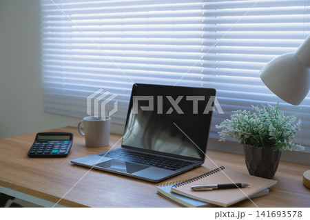 Laptop with Coffee Cup and Notebooks on Wooden Desk in Bright Home Office Workspace Laptop with Coffee Cup and Notebooks on Wooden Desk in Bright Home Office Workspace 141693578
