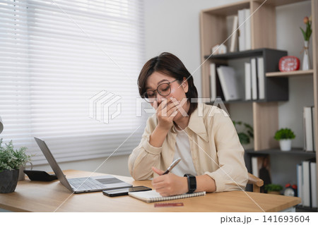 Asian woman hand using calculator with laptop on wooden desk in minimalist home office, focused on accounting work or freelance business 141693604