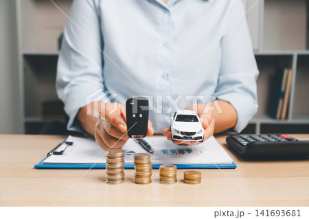 Business professional presenting car key and white toy car above coin stacks, representing vehicle ownership, car handover, auto loan approval, and transportation finance concept. Business professional presenting car key and white toy car above coin stacks, representing vehicle ownership, car handover, auto loan approval, and transportation finance concept. 141693681