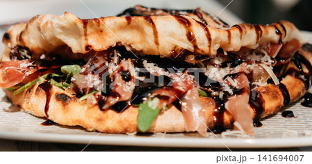 Crispy folded flatbread filled with prosciutto, greens and cheese, finished with balsamic glaze. Gourmet street food presentation creates a premium lunch concept 141694007